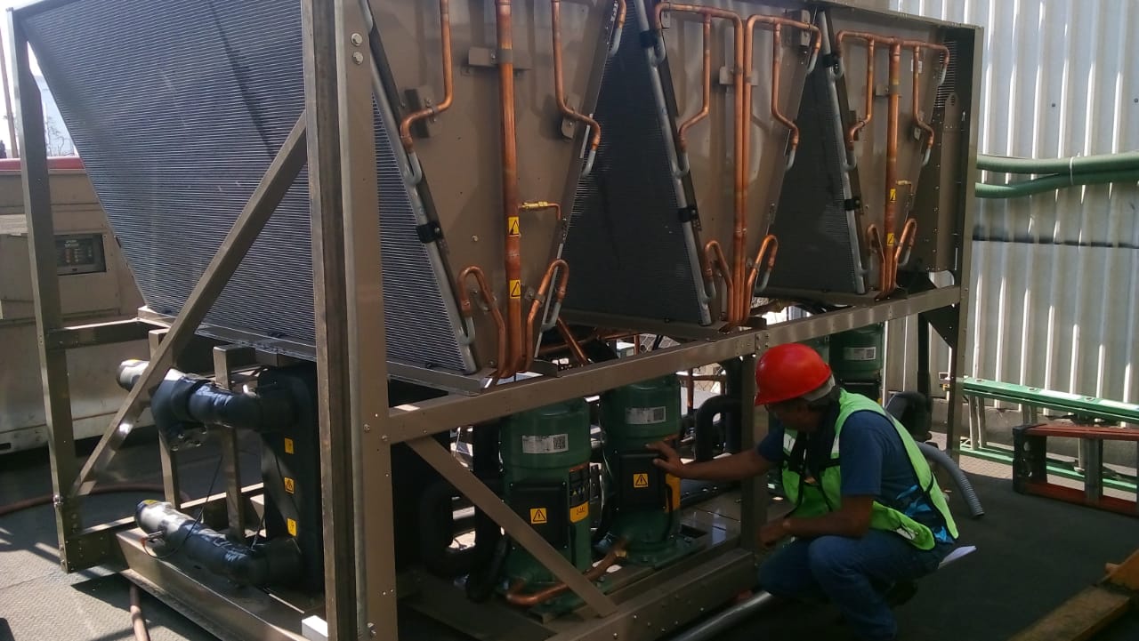 Técnico revisa los compresores y los serpentines de cobre en el interior de una unidad enfriadora industrial.