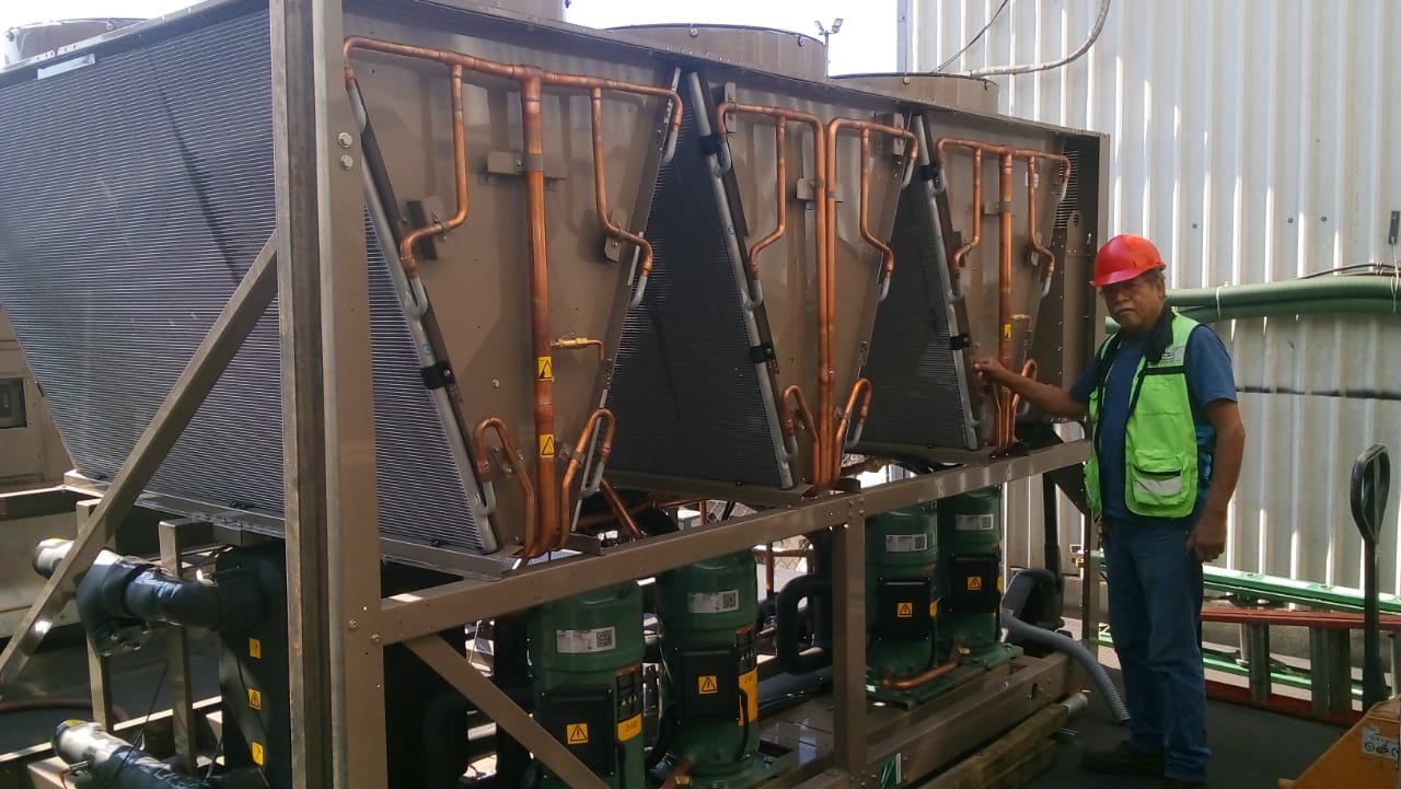 Técnico de SINTECSA junto a un sistema de refrigeración industrial con serpentines en V y tuberías de cobre expuestas.